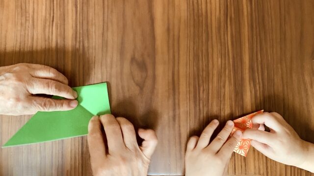 高齢者と子供の手で折り紙をするところ